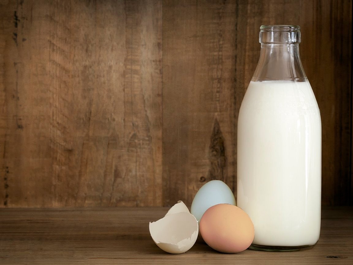 milk&eggs_milticolor Bottle of fresh milk next to a cracked eggshell and two colorful eggs on a wooden surface, highlighting essential ingredients for cooking and baking.